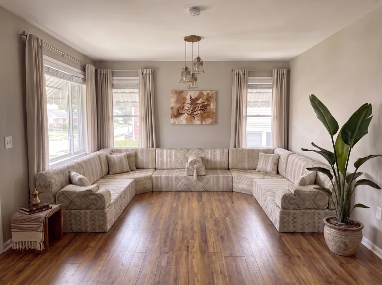 Beige flame-kilim U-shaped majlis sofa set on a bare wood floor in a grey living room with a tall plant