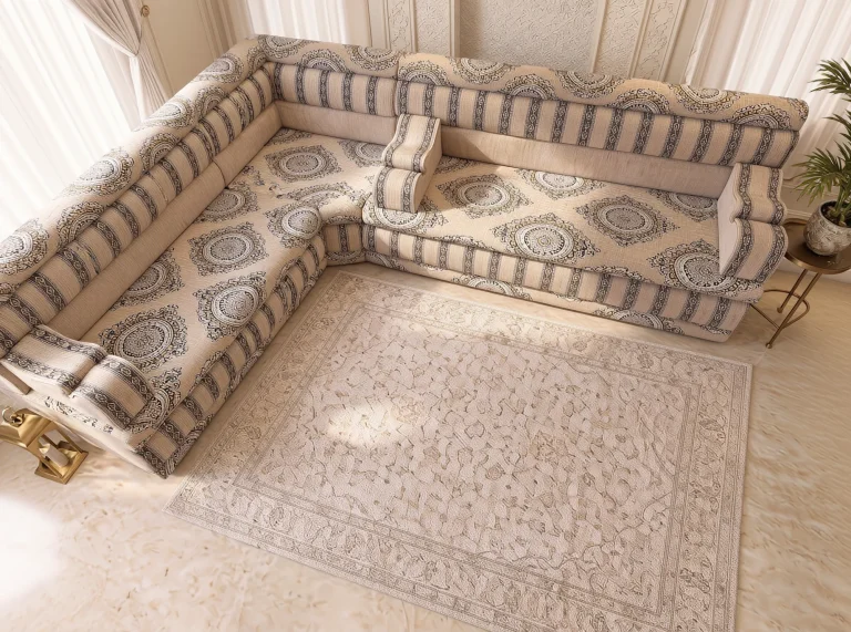 Overhead view of a beige L-shaped Arabic majlis with large charcoal medallions on the seat and a cream rug