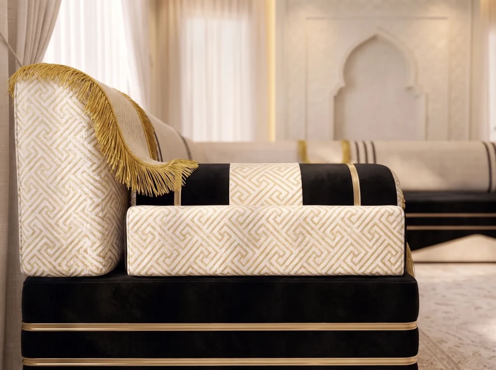 Side profile of a majlis sofa armrest in cream and gold key-pattern fabric on a black velvet seat
