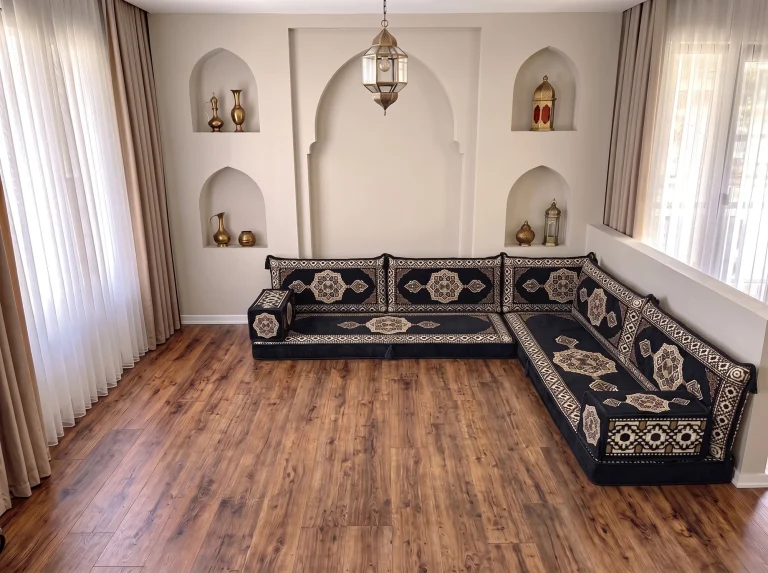 Black Arabic sofa with gold medallions in an L shape on a bare wooden floor in a room with arched wall niches