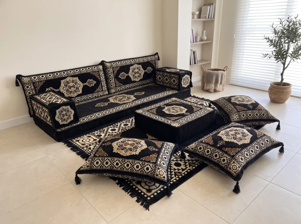 Angled view of a black and gold medallion floor seating set with ottoman and tasselled cushions on cream tiles