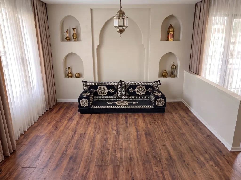 Black and gold medallion Arabic floor sofa with two back cushions and two armrests on a bare floor below arched niches