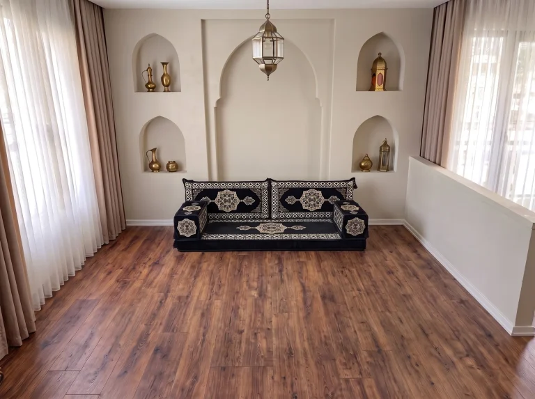 Black and gold medallion Arabic floor sofa with two back cushions and two armrests on a bare floor below arched niches