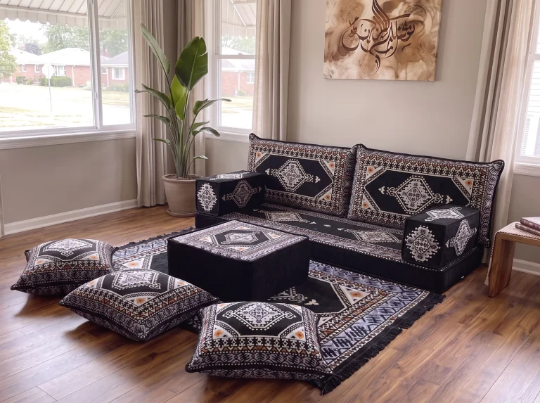 Close angled view of a black kilim Arabic sofa with ottoman, matching rug and three floor cushions by a window