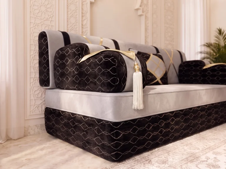 Close-up of a black velvet armrest with a gold flap and white tassel on a light grey majlis sofa