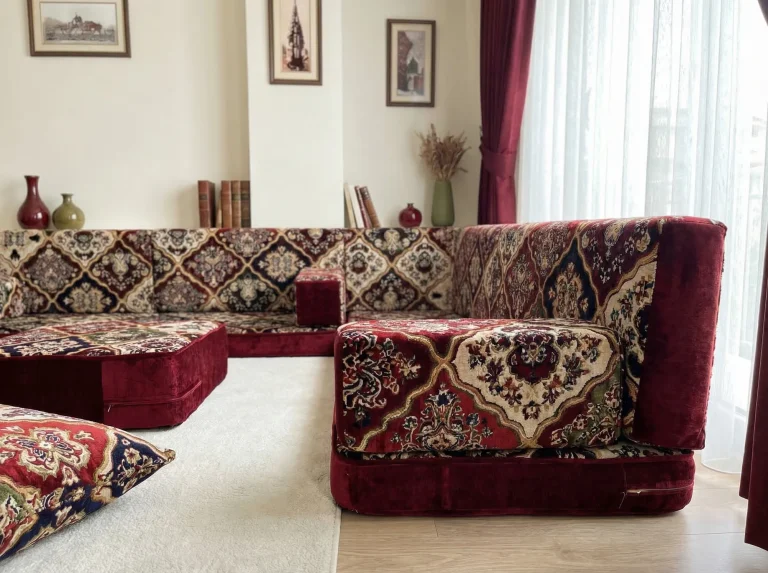 Low side view of a burgundy velvet Arabic floor sofa showing the armrest, base height and ottoman