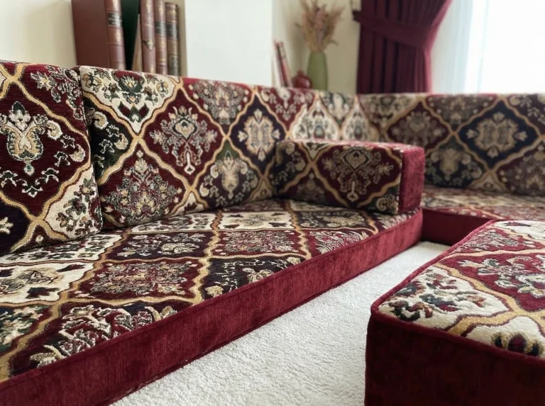 Close-up of a burgundy velvet diwan floor sofa seat with a woven diamond carpet pattern and plain velvet edge