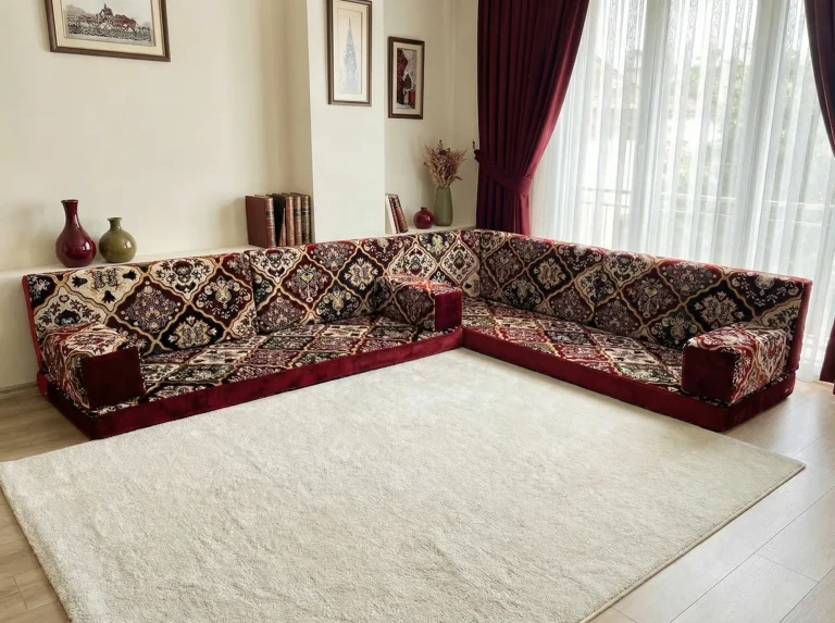 Burgundy velvet Arabic floor couch in an L shape with a diamond carpet pattern beside a bright curtained window