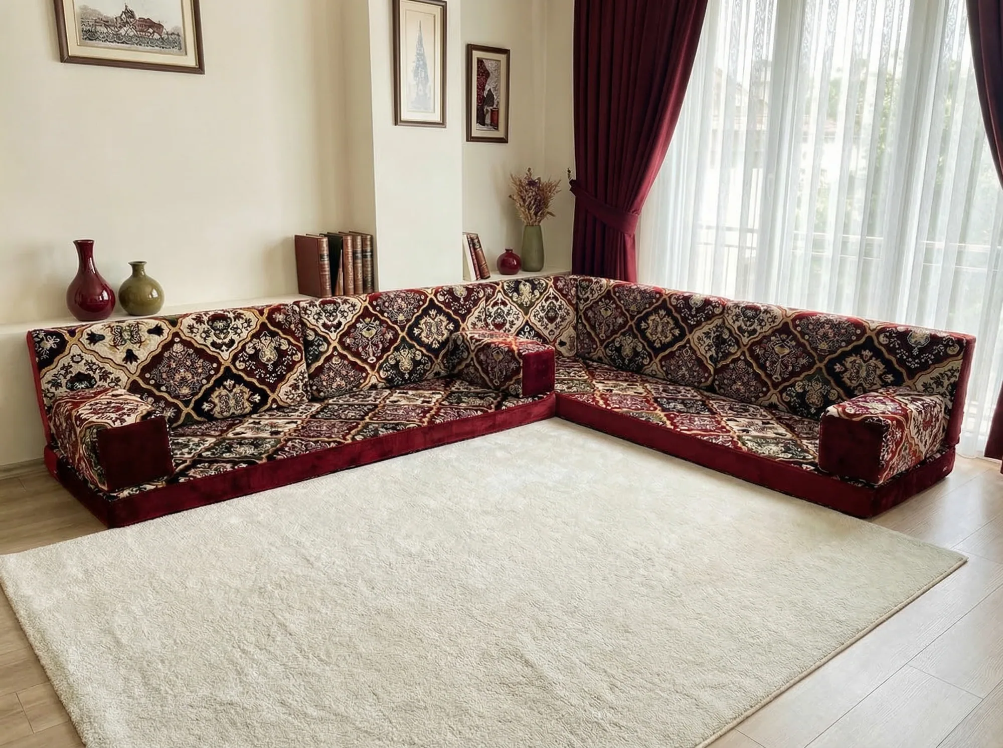 Burgundy velvet Arabic floor couch in an L shape with a diamond carpet pattern beside a bright curtained window