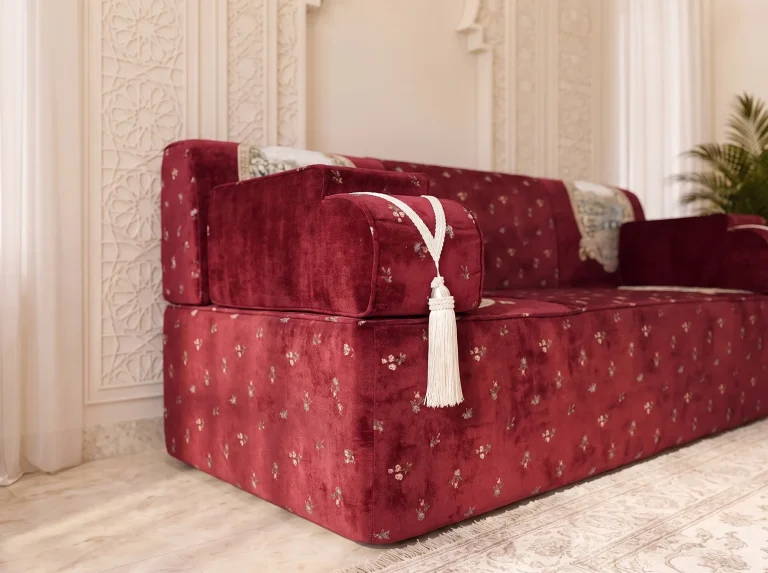 Close-up of a burgundy velvet armrest with a cream cord tassel on an Arabic majlis with gold floral sprigs