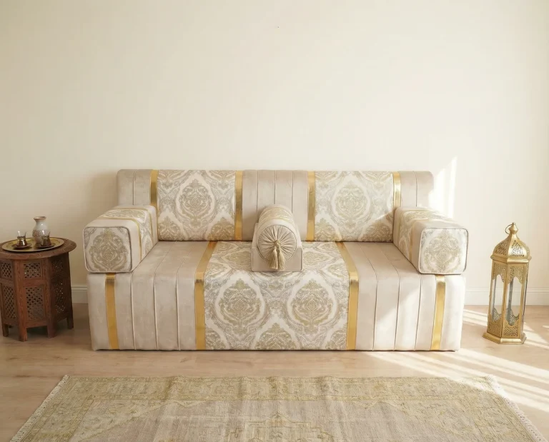 Ivory velvet diwan floor sofa with gold damask panels and gold stripes, beside a carved tea table and brass lantern