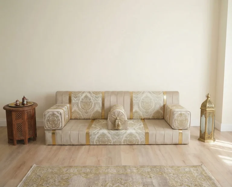 Low ivory velvet diwan floor sofa with gold damask panels sitting directly on a wood floor under a wide empty cream wall