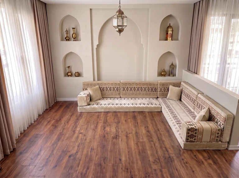Cream Arabic floor couch with burgundy cross-stitch bands in an L shape on a bare wood floor by arched niches