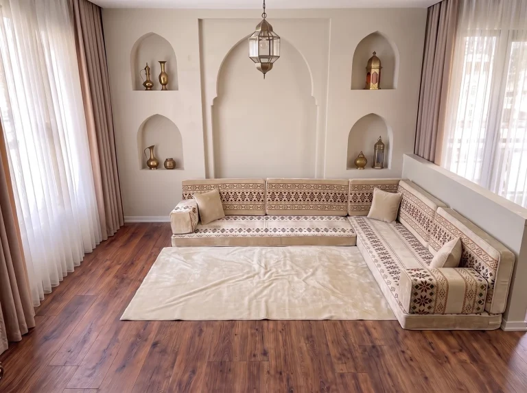 Cream velvet Arabic floor sofa with burgundy cross-stitch bands in an L shape with a plain cream rug by arched niches
