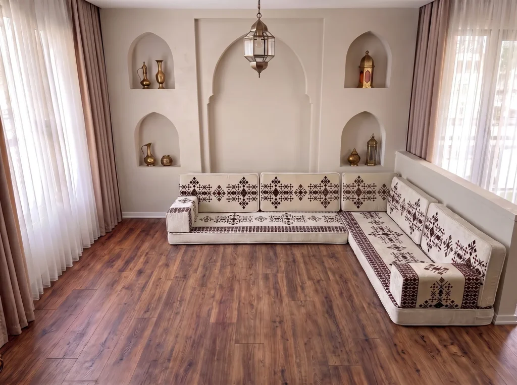 Cream Arabic floor sofa with burgundy sadu motifs in an L shape on a dark wooden floor below arched niches