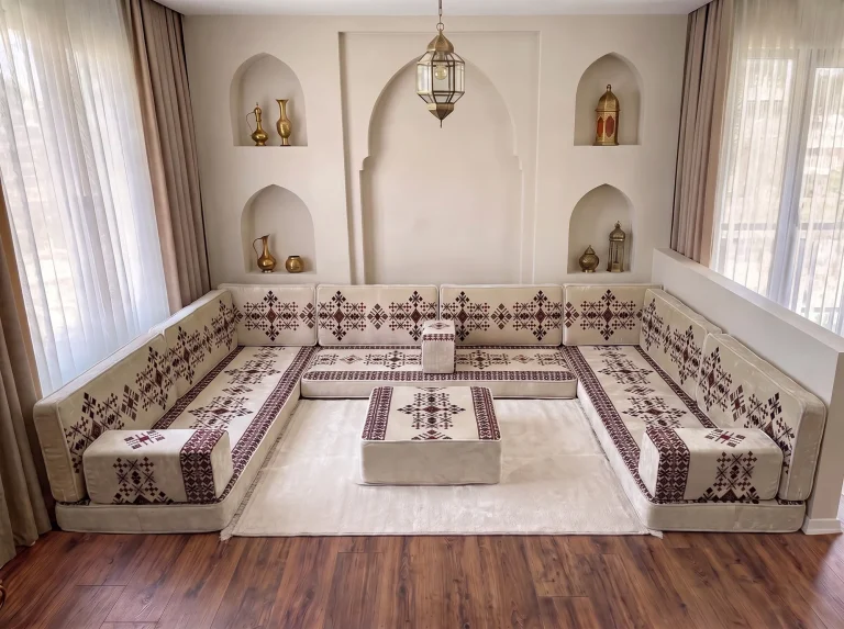 Cream sadu Arabic floor couch in a U shape with a sadu-topped ottoman on a cream rug at its centre