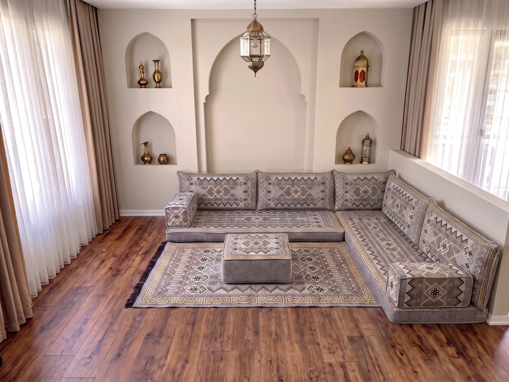 Gray and gold Arabic floor couch in an L shape with a matching ottoman on a fringed gray rug in an arched room