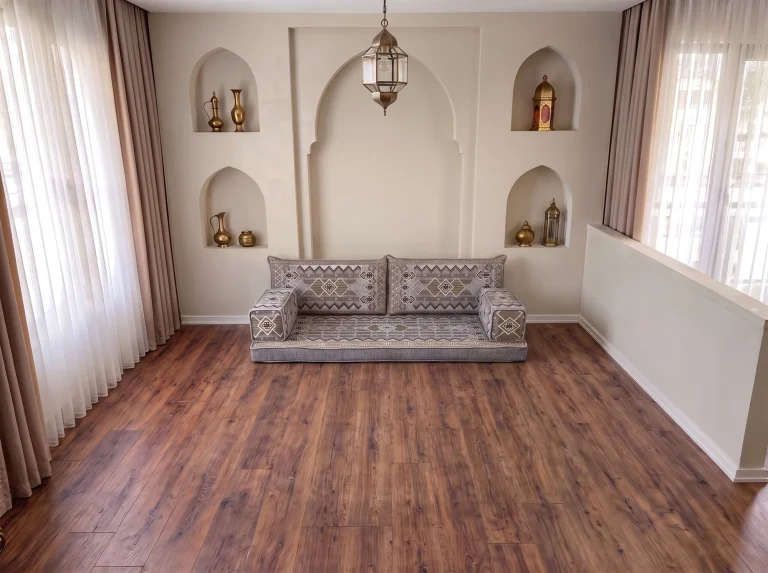 Low gray and gold kilim-pattern floor seating set as a single row on a bare wood floor in a room with arched wall niches