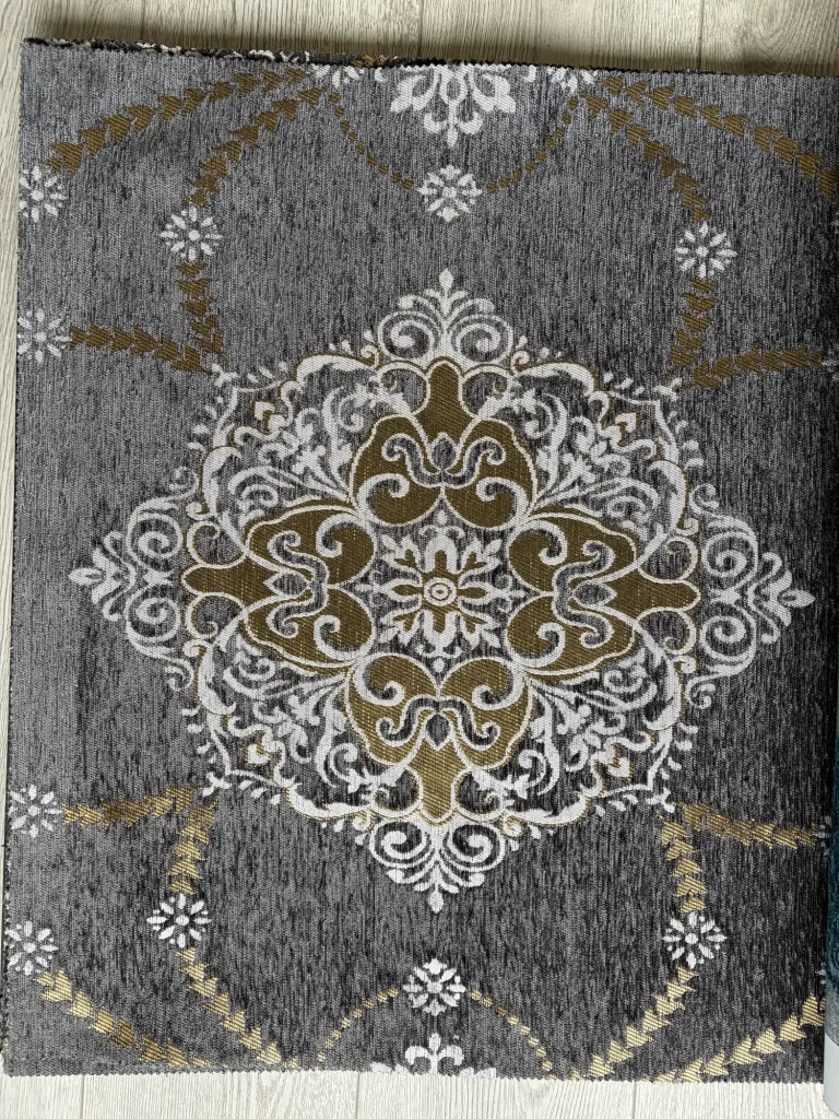 Grey chenille upholstery fabric swatch with one large white and gold medallion and leaf garlands