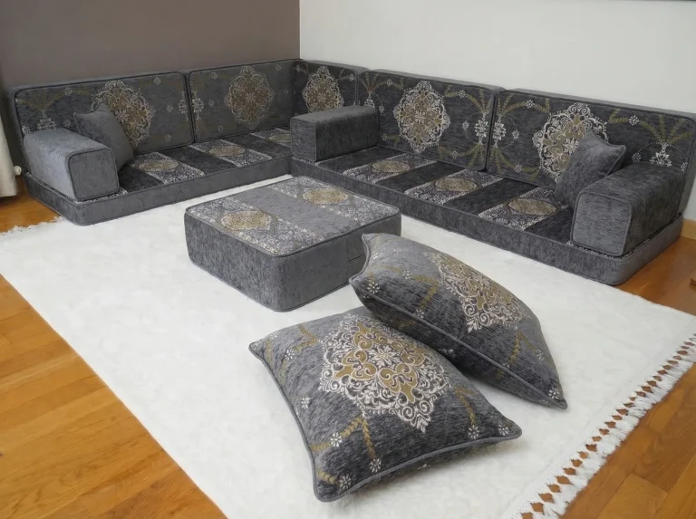 Grey floor seating set in an L shape with gold medallion back cushions and an ottoman on a white rug