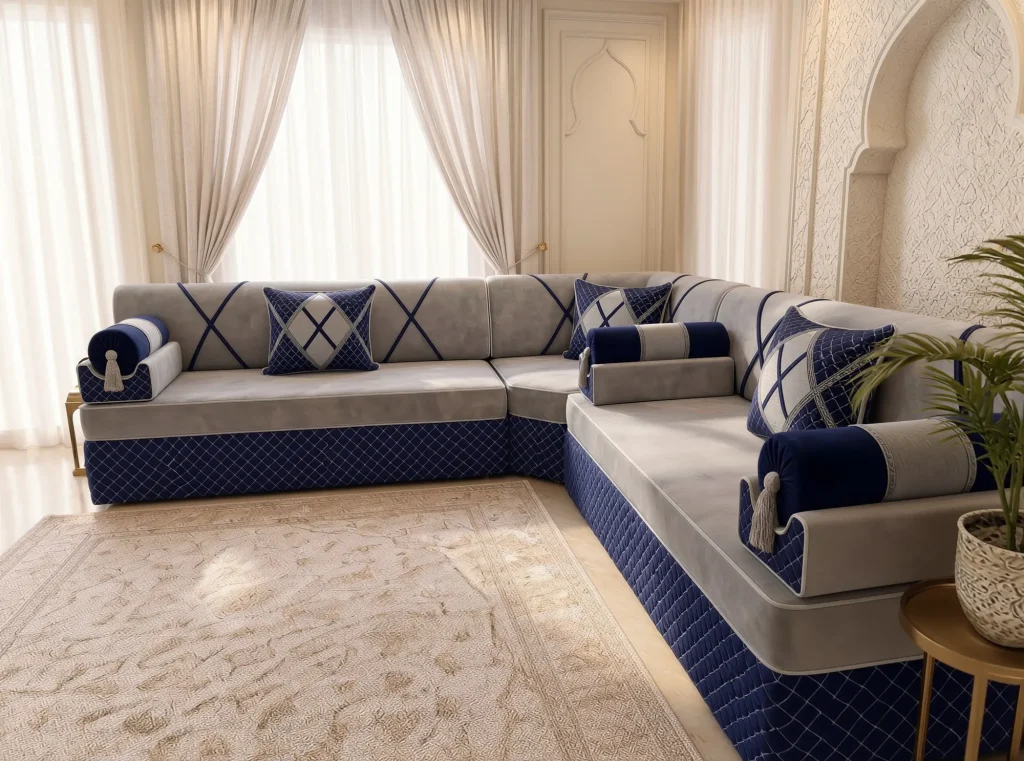 Light grey velvet L-shaped majlis sofa with navy bolster armrests seen along the right arm