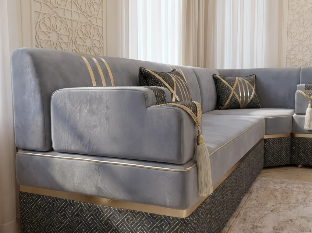 Close-up of a grey velvet armrest with a cream tassel on a majlis sofa with gold trim and a black base