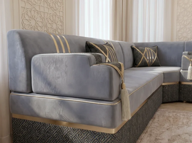 Close-up of a grey velvet armrest with a cream tassel on a majlis sofa with gold trim and a black base