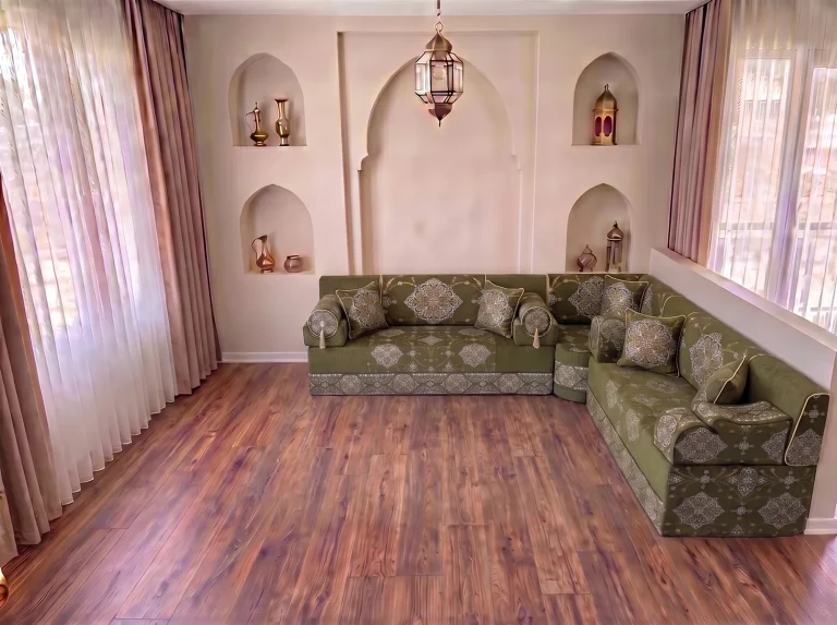 Khaki green medallion-damask majlis sofa set with bolster armrests in an L shape on a bare wood floor by arched niches