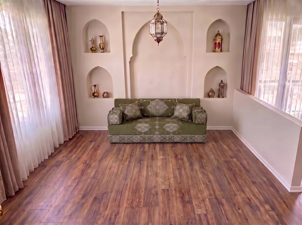 Khaki green medallion-damask Arabic jalsa with bolster armrests as a single row on a bare wood floor by arched niches