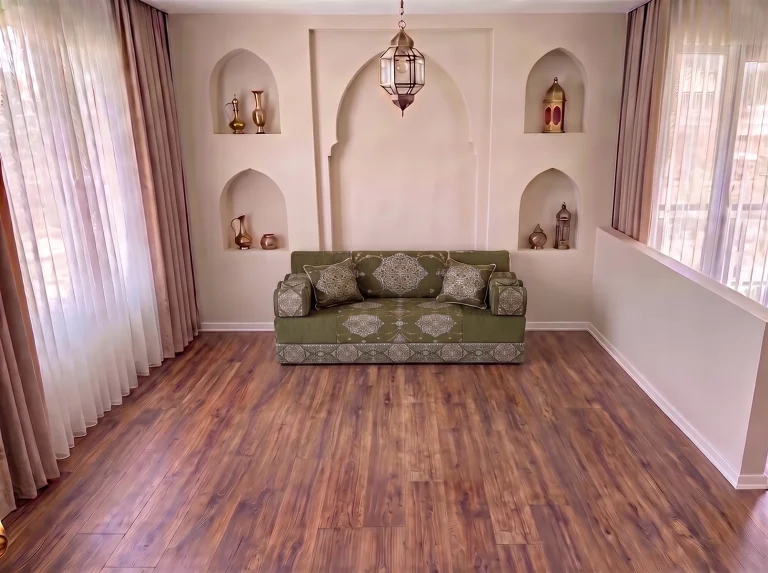 Khaki green medallion-damask Arabic jalsa with bolster armrests as a single row on a bare wood floor by arched niches