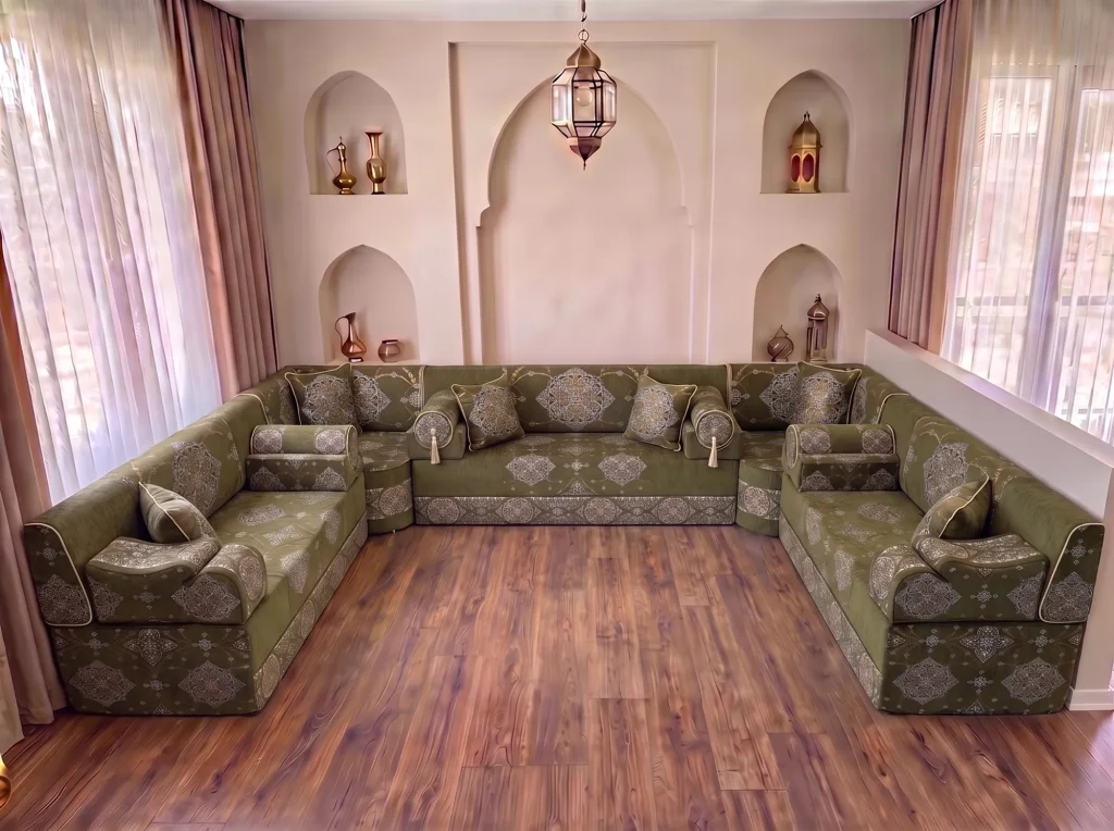 Khaki green medallion-damask majlis seating with bolster armrests in a U shape on a bare wood floor by arched niches
