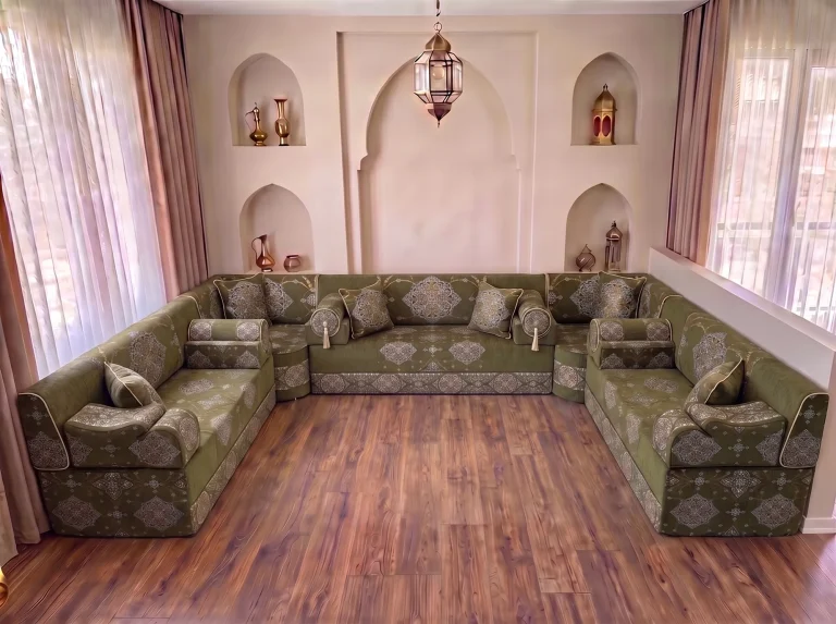 Khaki green medallion-damask majlis seating with bolster armrests in a U shape on a bare wood floor by arched niches
