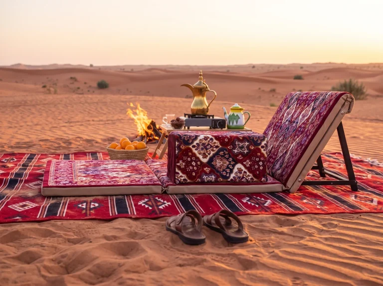 Side view of a maroon patterned Arabic sunbed lounger on a striped kilim beside a small desert campfire