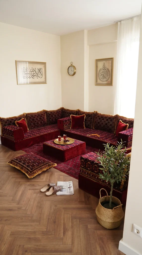 Maroon velvet Arabic floor sofa with gold fringe along three sides of a room with Arabic calligraphy frames