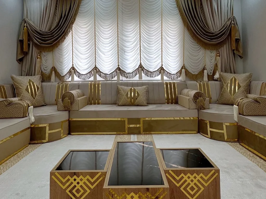 Beige velvet majlis sofa with gold-striped backs and key-pattern pillows facing three black-glass tables
