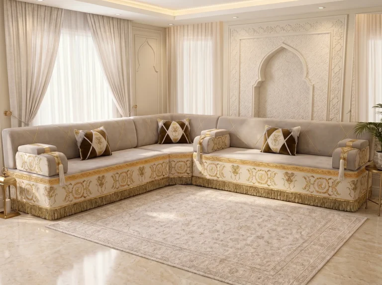 Beige majlis sofa in an L shape with gold-embroidered cream bases and gold fringe on a beige rug before a carved arch