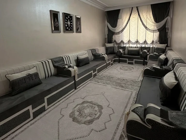 Black and cream striped majlis seating lining a narrow room on three sides, with fringed pillows and a grey medallion rug