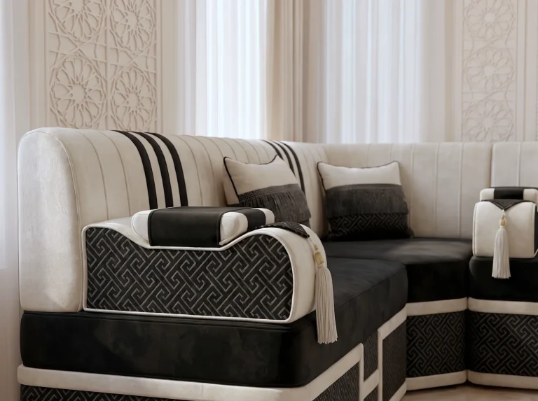 Close-up of a shaped armrest in black key-pattern jacquard with cream piping and a tassel on a black velvet majlis sofa