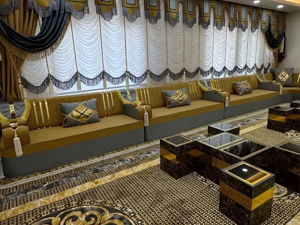 Long mustard and grey majlis sofa with gold-striped backs along a window wall, with dark marble-effect cube tables in front