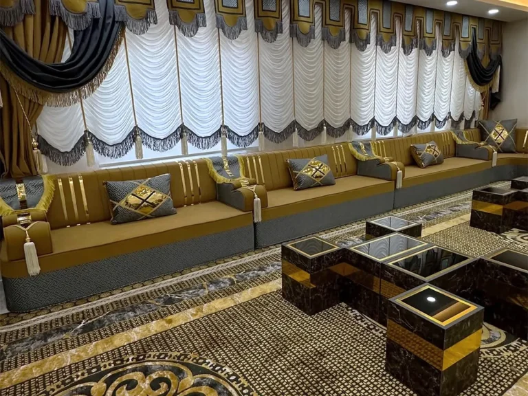 Long mustard and grey majlis sofa with gold-striped backs along a window wall, with dark marble-effect cube tables in front
