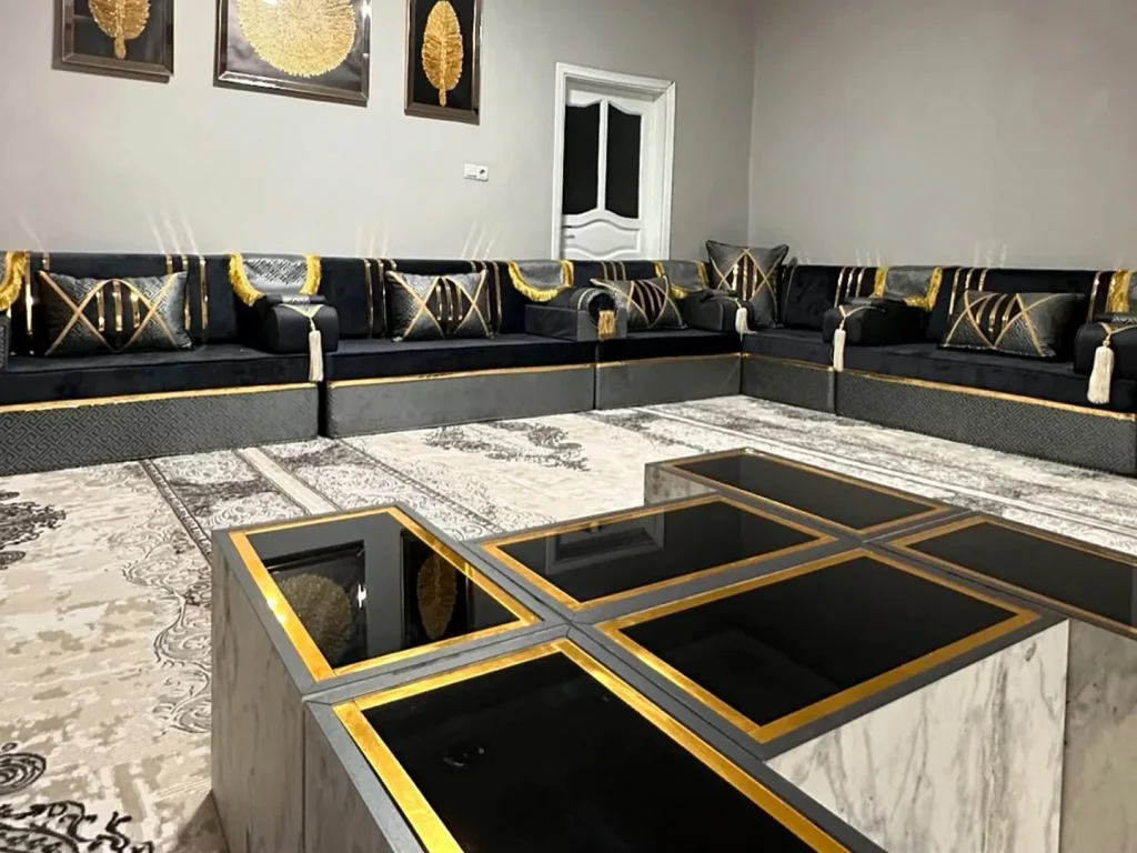 Black velvet majlis seating with gold piping photographed across a cluster of gold-edged marble tables