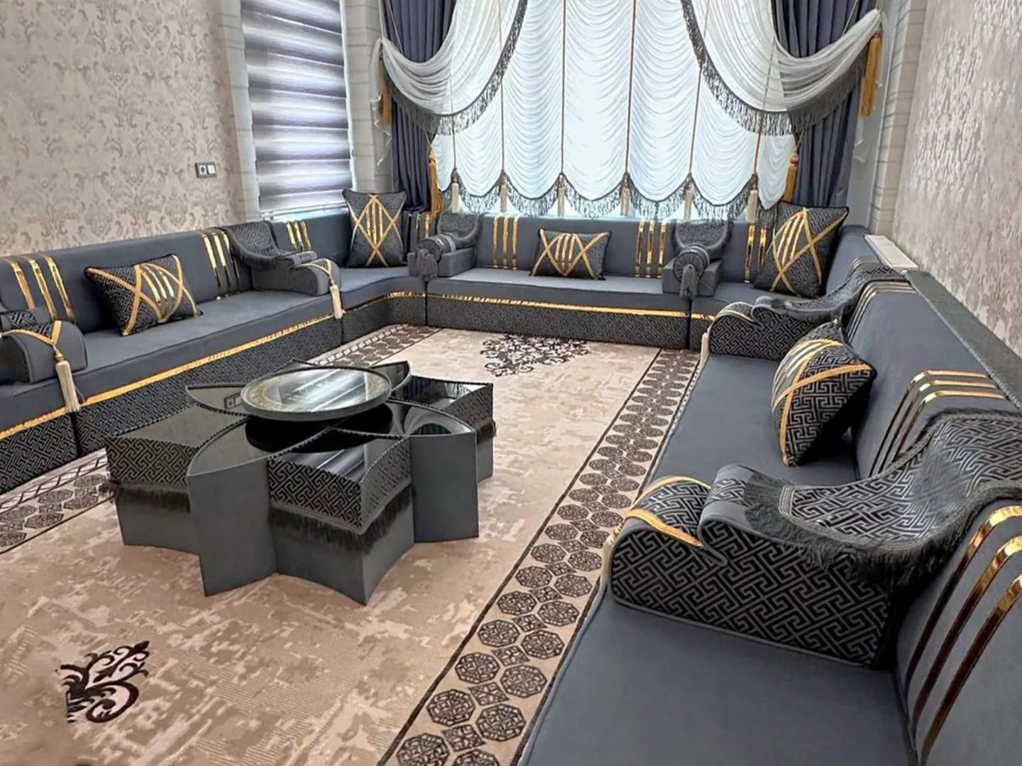 Slate grey majlis sofa set with gold stripes and black key-pattern trim around a grey star-shaped table on a beige rug