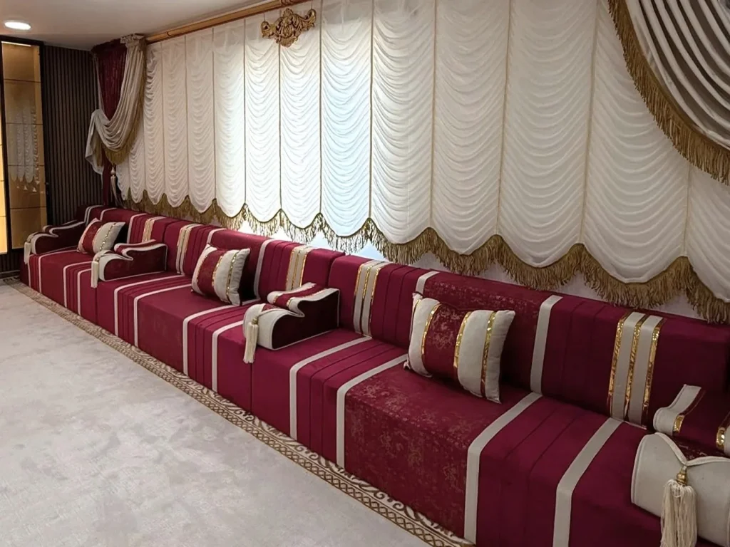 A single unbroken row of burgundy velvet majlis seating along a window wall, the kind of continuous run that makes a head wall