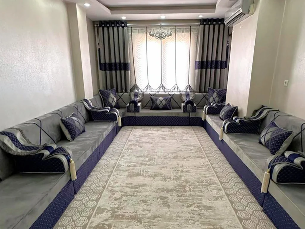 Light grey Arabic majlis on navy quilted bases lining three walls of a narrow room, with navy armrests and a beige rug