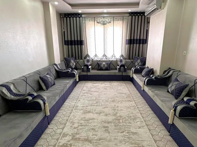Light grey Arabic majlis on navy quilted bases lining three walls of a narrow room, with navy armrests and a beige rug