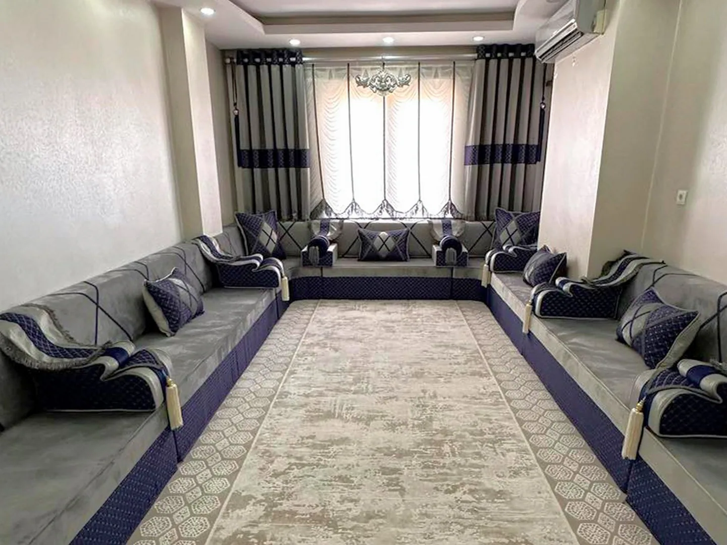 Light grey Arabic majlis on navy quilted bases lining three walls of a narrow room, with navy armrests and a beige rug