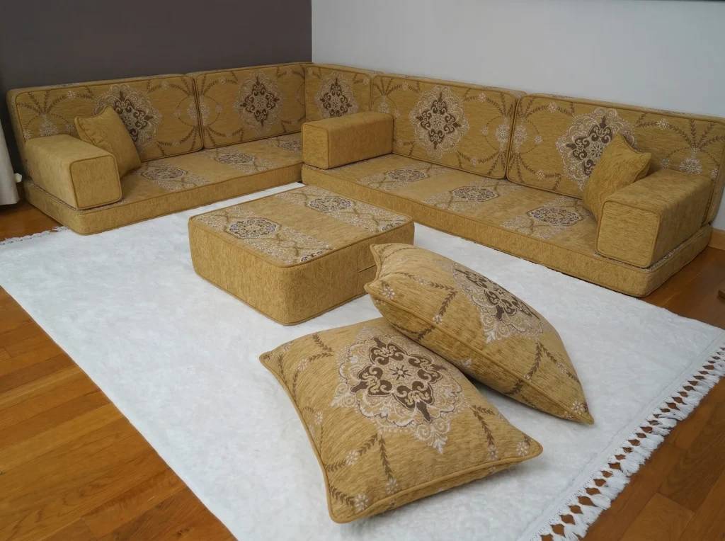 Mustard yellow Arabic floor sofa in an L shape with brown medallion cushions and an ottoman on a white rug