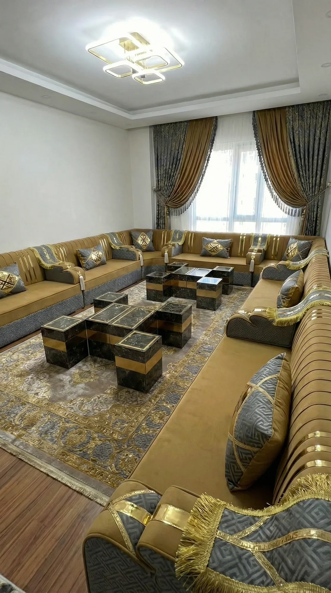 Mustard velvet majlis sofa set with gold-striped backs and grey key-pattern bases around dark marble-effect tables