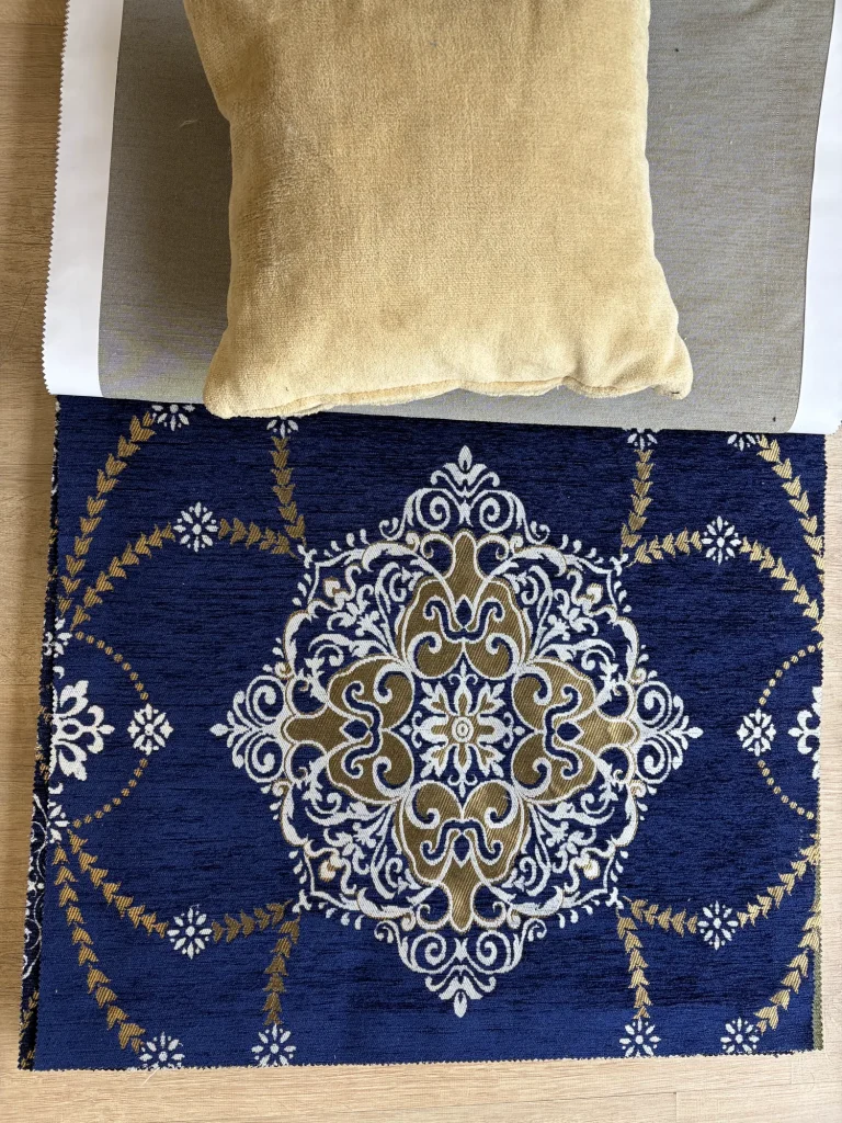 Navy chenille upholstery fabric swatch with one large white and gold woven medallion, beside a mustard cushion