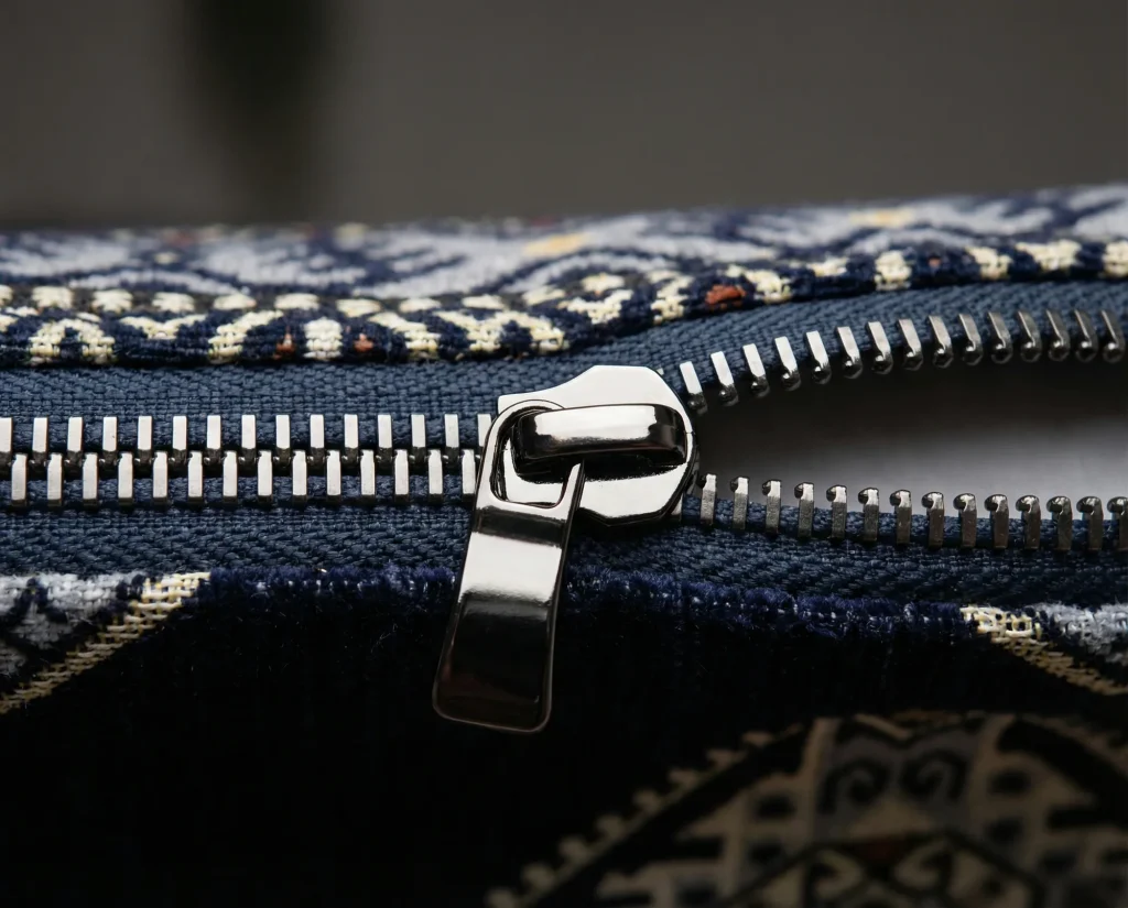 Macro of a polished metal zip slider and teeth on a navy and cream patterned upholstery cushion cover
